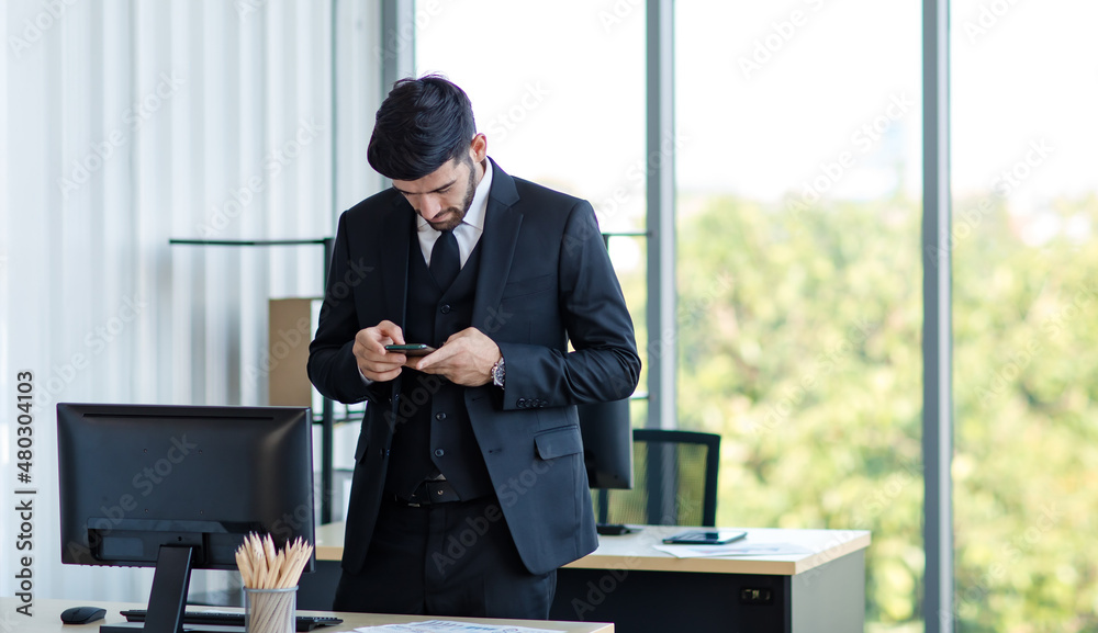 Caucasian stressed depressed upset unhappy blonde hair male businessman employee in blue formal suit with necktie holding looking at smartphone in hand at working desk with computer in company office Caucasian stressed depressed upset unhappy blonde hair male businessman employee in blue formal suit with necktie holding looking at smartphone in hand at working desk with computer in company office