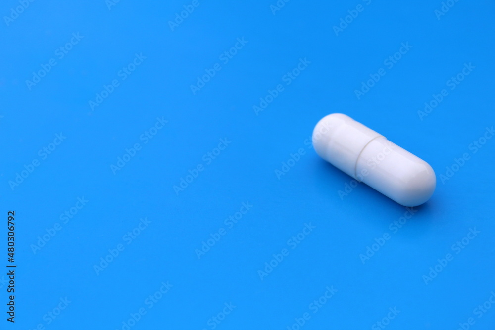 The drug in a white capsule lies alone on an isolated blue background. The drug in a white capsule lies alone on an isolated blue background.