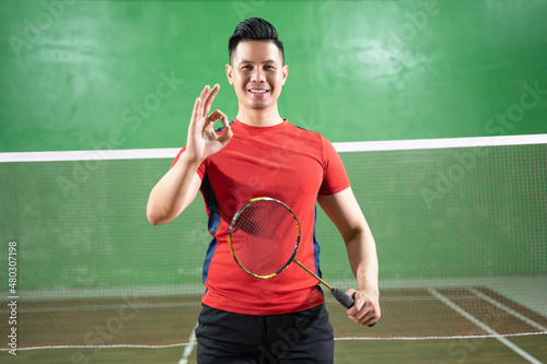 Smiling male badminton player holding racket with okay hand gesture © Odua Images