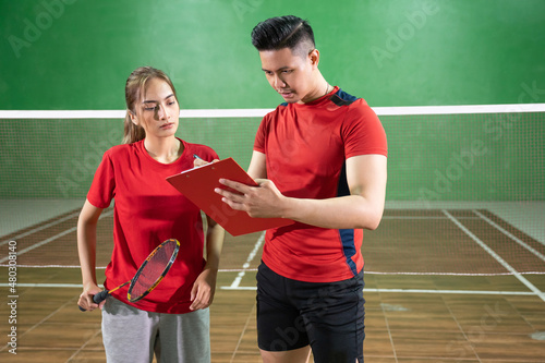 Female badminton player paying attention to coach's instructions with clipboard