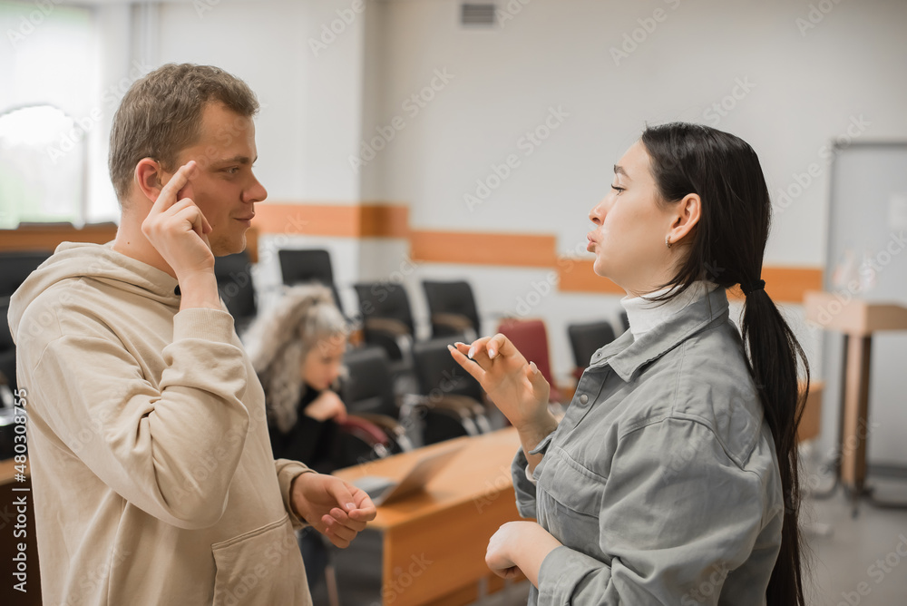 Obraz premium The girl and the guy talk in sign language. Two deaf students chatting in a university class.