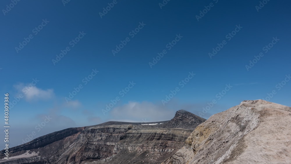 The edge of the volcano crater against a clear blue sky. The layered structure of the soil is visible.  Copy space. Kamchatka. Gorely Volcano