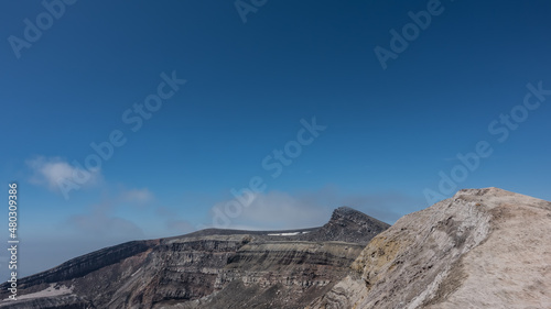 The edge of the volcano crater against a clear blue sky. The layered structure of the soil is visible. Copy space. Kamchatka. Gorely Volcano
