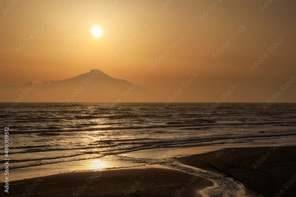 夕陽に染まる海と山影に沈む太陽
