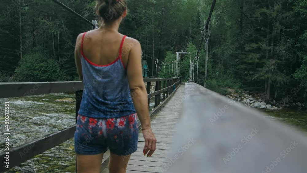 Woman Walking Along Suspension Bridge Alone in Picturesque Green Forest Setting. Woman Walking Along Suspension Bridge Alone in Picturesque Green Forest Setting.