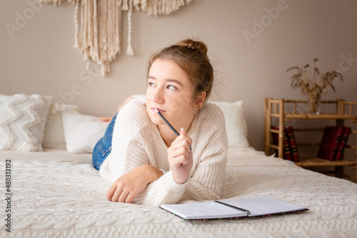 Closeup portrait of a relaxed young girl writing book while lying on the bed
