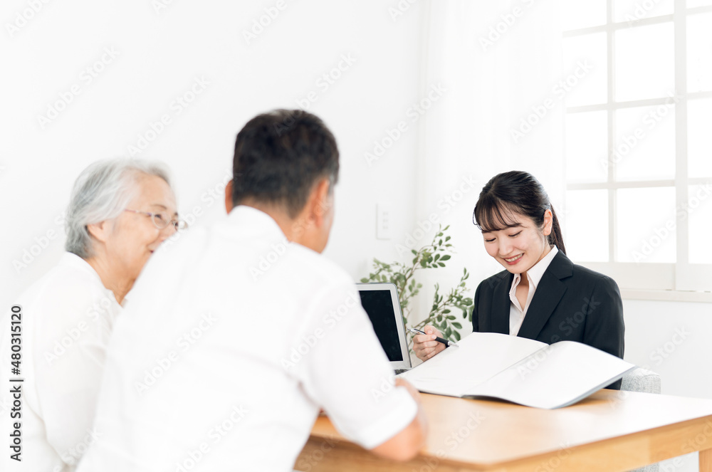 資料で説明するスーツ姿の女性と高齢者夫婦
