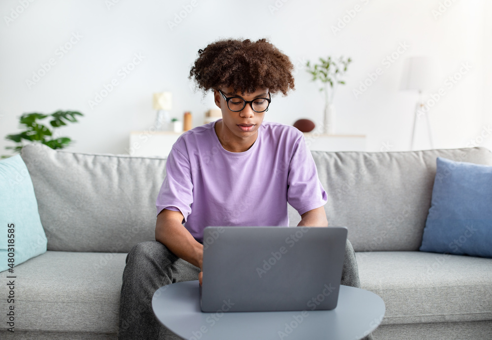 Intelligent black teen guy studying remotely from home, uing laptop pc, writing online test. Distance education