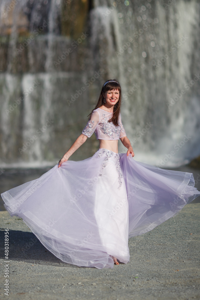 a beautiful young girl in a magnificent dress dances against the backdrop of a waterfall, a story about a forest elf
