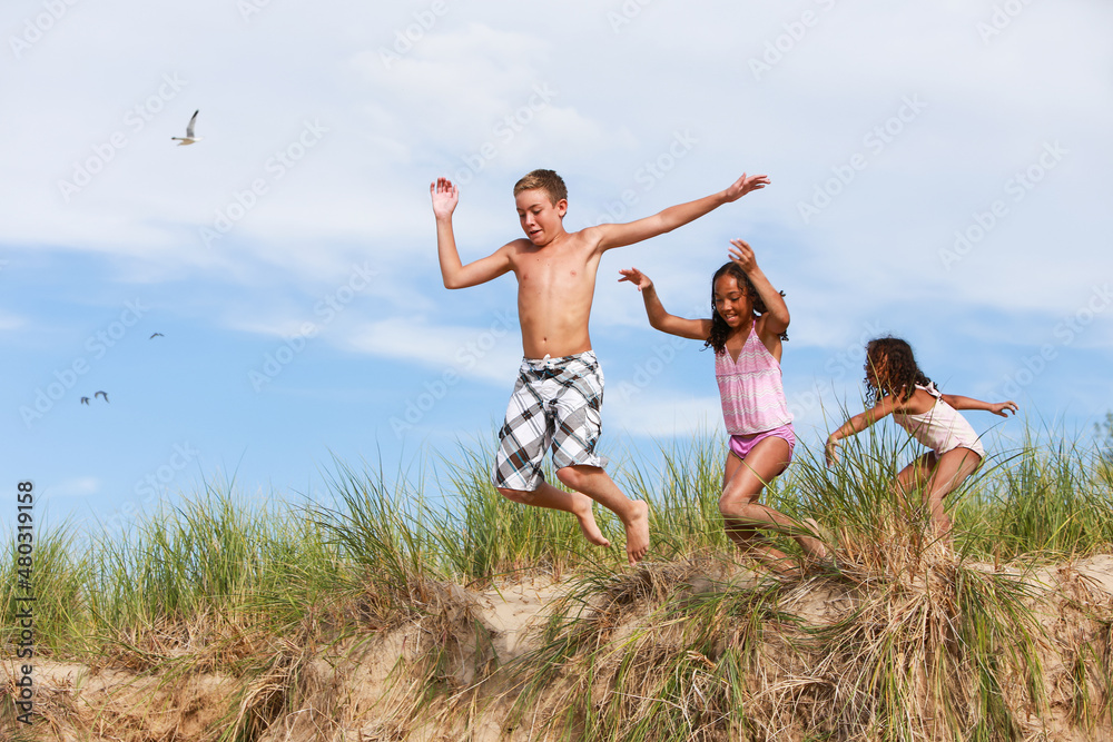 Children jumping off of sand dunes at the beach Children jumping off of sand dunes at the beach