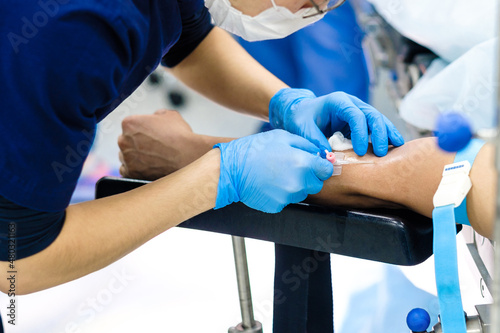 The doctor inserts a dropper needle into a vein in the patient s arm. Selective focus. Doctor in sterile gloves and a protective mask. Intravenous administration of drugs through a catheter. 