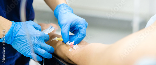 Inserting the dropper needle into the patient's arm. Selective focus. Doctor's hands in sterile gloves install a catheter for intravenous administration of drugs to a patient. Widescreen image. photo