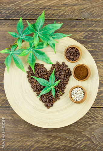 an original composition of hearts, leaves and seeds of connabis laid out of coffee beans on a bamboo dish and a wooden table. top vertical view.