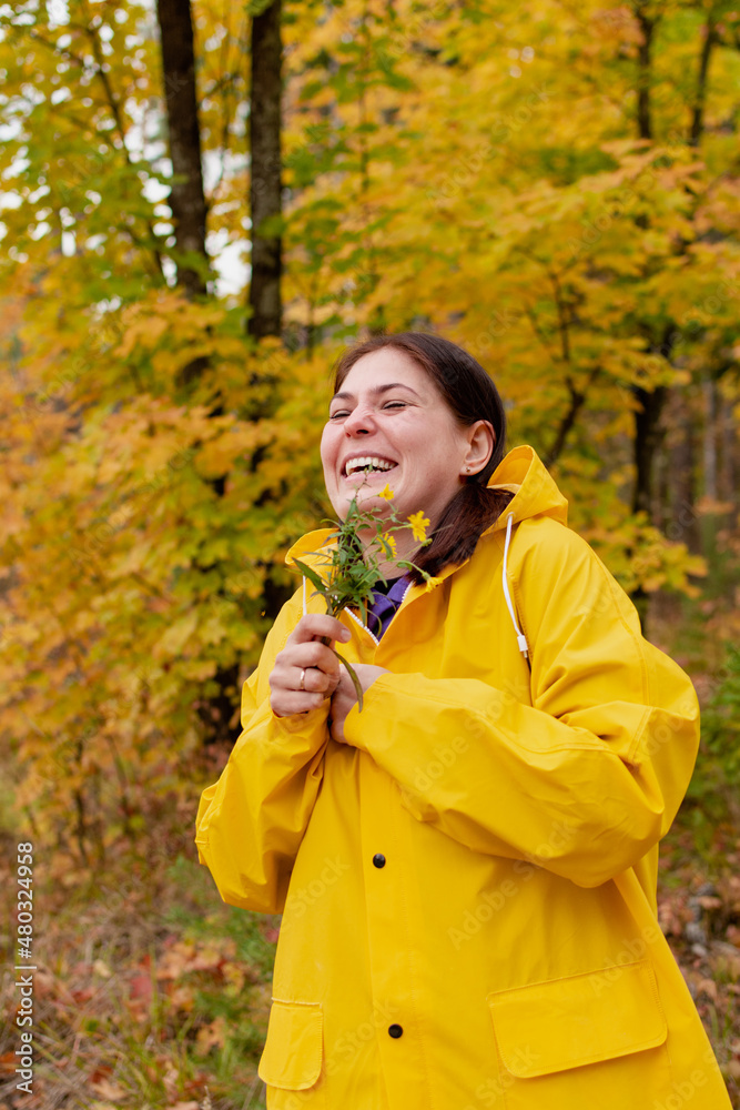 A cheerful young woman in a yellow raincoat and yellow boots on the background of an autumn landscape A cheerful young woman in a yellow raincoat and yellow boots on the background of an autumn landscape