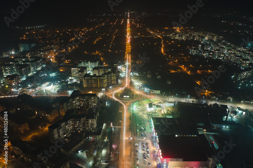 Aerial view of high rise apartment buildings and bright illuminated roundabout intersection on urban street in city residential area at night. Dark urban landscape