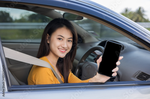 Young Asian woman smiling drives a beautiful nature on the road. She showing blank screen smartphone. Female using cell phone navigation for driving location