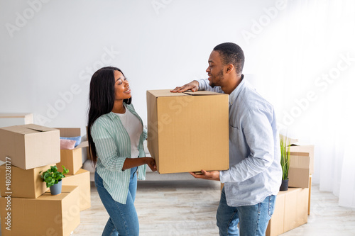 Happy young black couple carrying cardboard box together, helping each other on moving day, free space