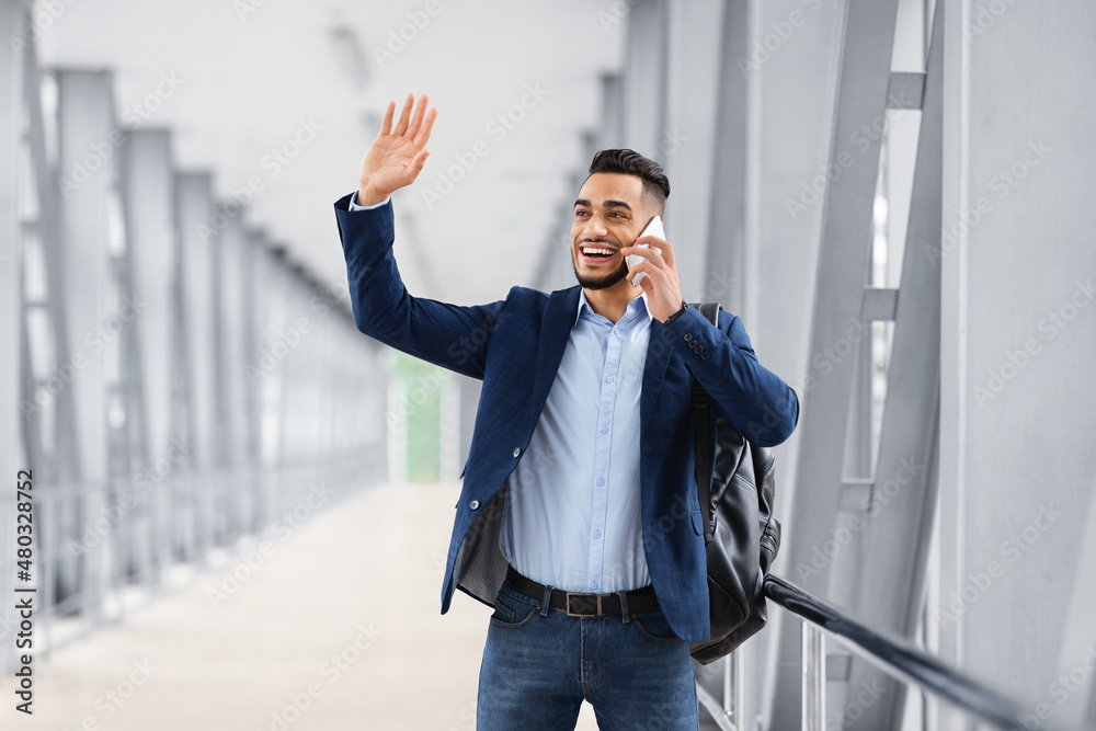 Arab Man Waving Hand And Talking On Cellphone While Walking In Airport Arab Man Waving Hand And Talking On Cellphone While Walking In Airport