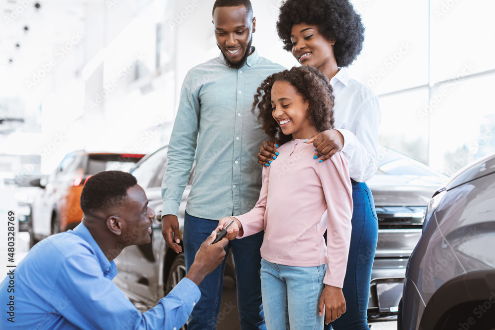 Happy black family buying new car, salesman giving them key at auto dealership Happy black family buying new car, salesman giving them key at auto dealership