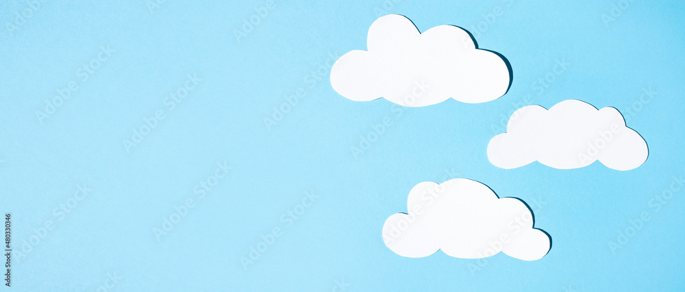 Silhouettes of clouds from white paper on a blue background. Banner, flat lay, place for text.