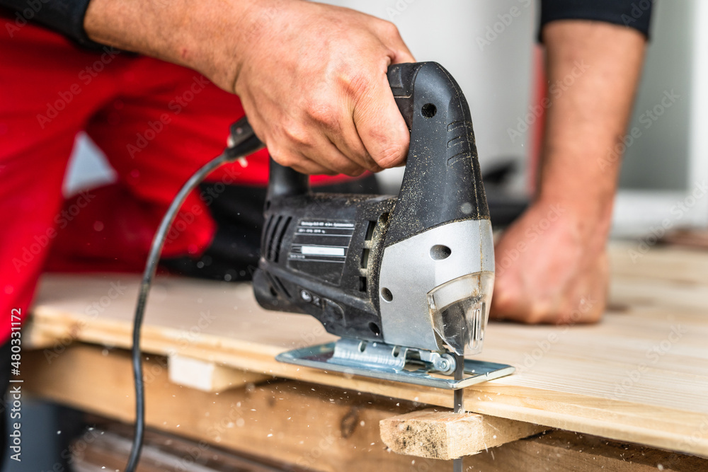 Close up on hand of unknown carpenter working with an electric jigsaw cutting wood with saw woodworking hobby concept Close up on hand of unknown carpenter working with an electric jigsaw cutting wood with saw woodworking hobby concept