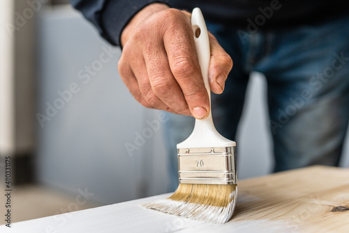 Fototapeta Naklejka Na Ścianę i Meble -  Close up on white paint brush in the hand of unknown man painting wooden board hobby and renovation repairing concept
