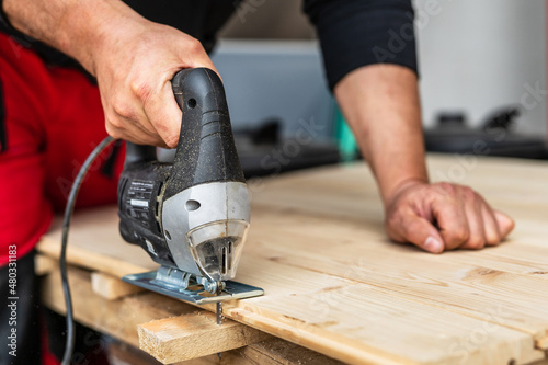 Photos Close up on hand of unknown carpenter working with an electric jigsaw cutting wo