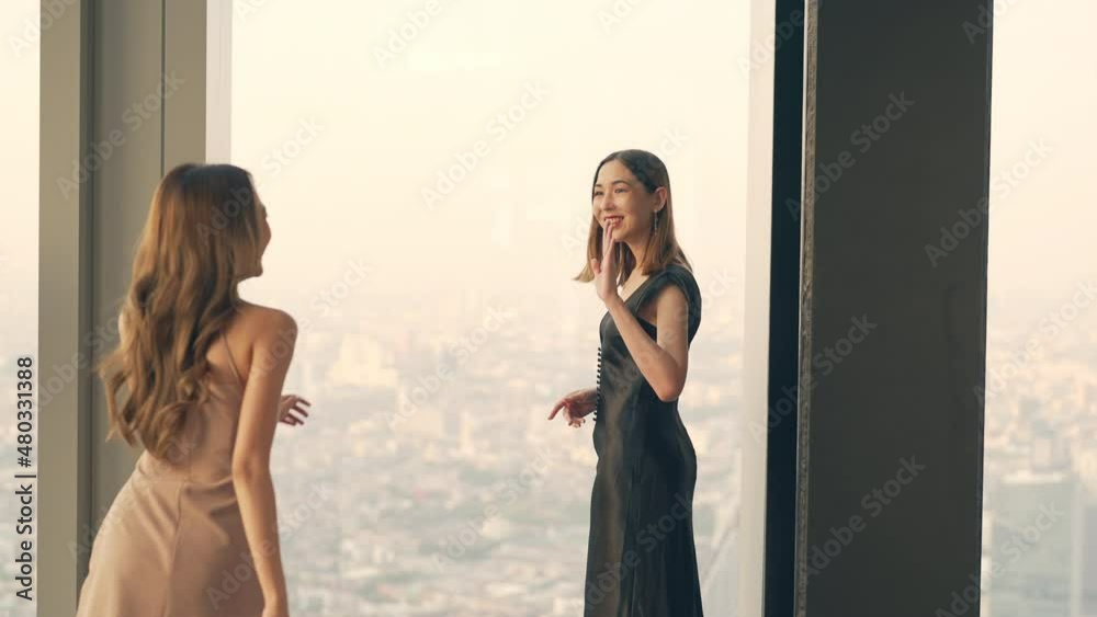 Beautiful Asian woman friends meeting and talking together at skyscraper rooftop restaurant in metropolis at summer sunset. Smiling female friend enjoy outdoor lifestyle activity in the city at night