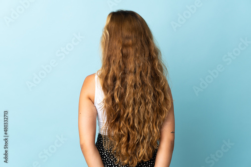 Young blonde woman isolated on blue background in back position and looking back