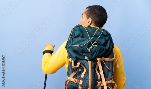 African American man with backpack and trekking poles over isolated background in back position and looking side photo