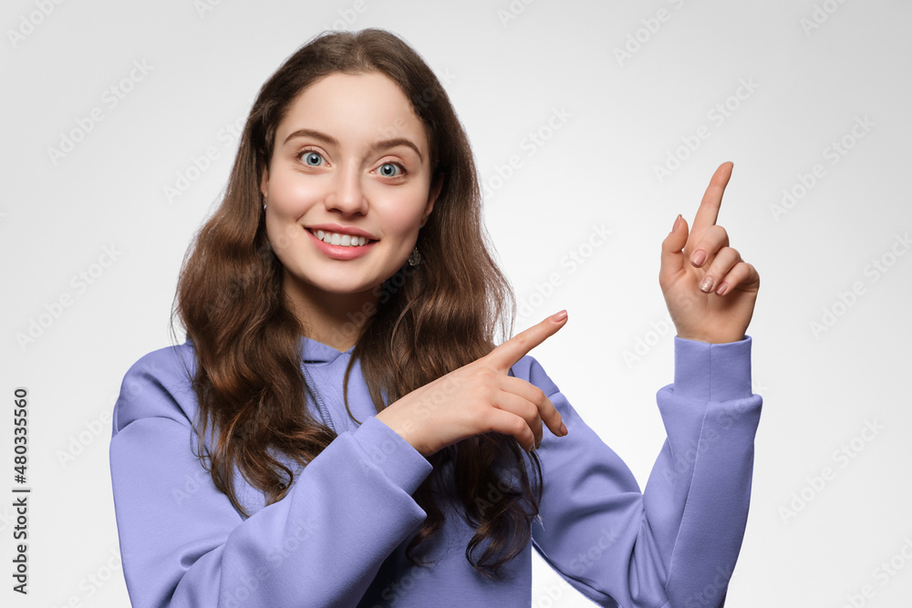 A young woman with long hair and blue eyes points her finger to the right side. The girl is wearing a violet oversized hoodie A young woman with long hair and blue eyes points her finger to the right side. The girl is wearing a violet oversized hoodie