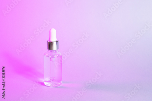 Facial serum in transparent glass bottle with dropper in pink neon gradient light. Cosmetic product for branding closeup. Trendy skin product advertising. Front view, copy space.