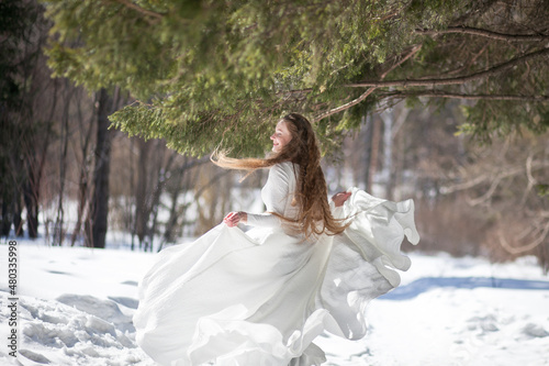 blonde with long hair, a girl in a long white dress walks in the winter forest, the snow queen, the bride with a bouquet of dianthus