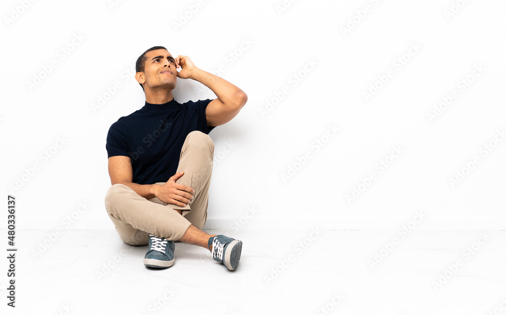 Fototapeta premium African American man sitting on the floor having doubts and with confuse face expression