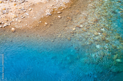 Riverside Landscape Detail / Stony natural riverbank and clear shallow blue water seen from above (copy space)