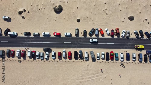 Static top-down view of parked cars by the road with slow-moving cars and resting tourists on the yellow sand on a hot day photo
