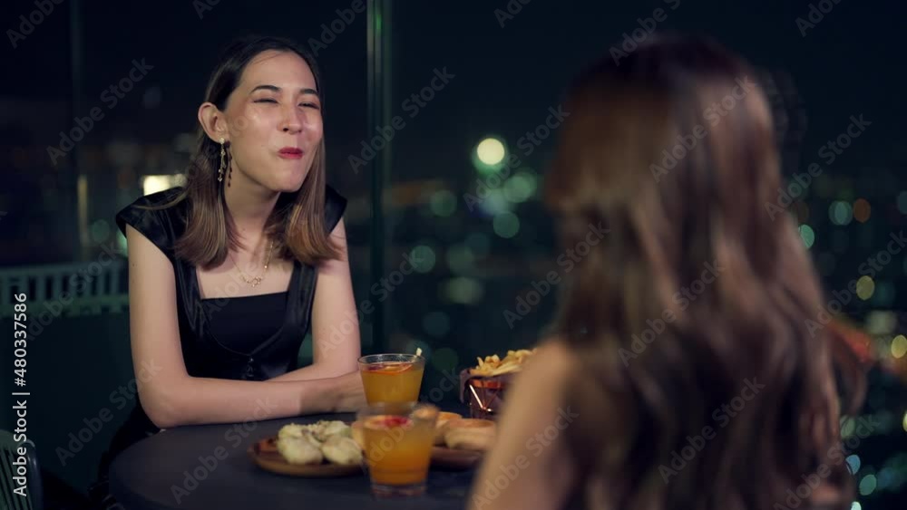 4K Two beautiful Asian woman friends meeting and dinner with cocktail drink together at skyscraper rooftop restaurant at night. Female friend enjoy outdoor lifestyle activity nightlife in the city. 4K Two beautiful Asian woman friends meeting and dinner with cocktail drink together at skyscraper rooftop restaurant at night. Female friend enjoy outdoor lifestyle activity nightlife in the city.