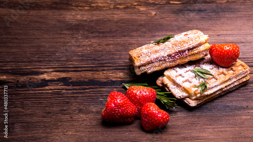 Wafers with marmalade and strawberries sprinkled with powder on an old wooden table, side view, copy space,