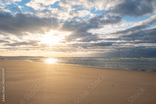 Amazing colorful sunset on a sandy beach at the sea under a sky painted with clouds and a golden sun. Picturesque nature scenery.Clouds reflected in water. Zen-like tranquil atmosphere no people