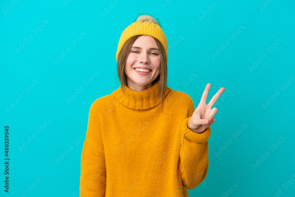 Fototapeta premium Young English woman wearing winter jacket isolated on blue background smiling and showing victory sign