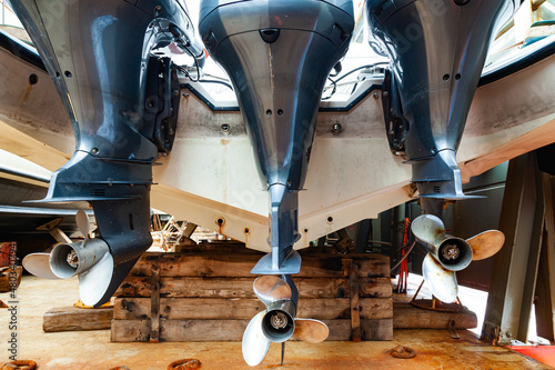 Fotografie, Obraz Three outboard motors mounted on a mount at the stern of a dry docked boat