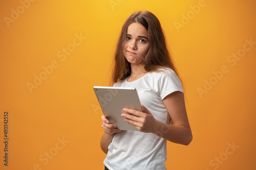 Beautiful teen girl using digital tablet over yellow studio background