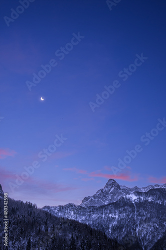 Crescent waning moon in purple sky overy mountain peaks