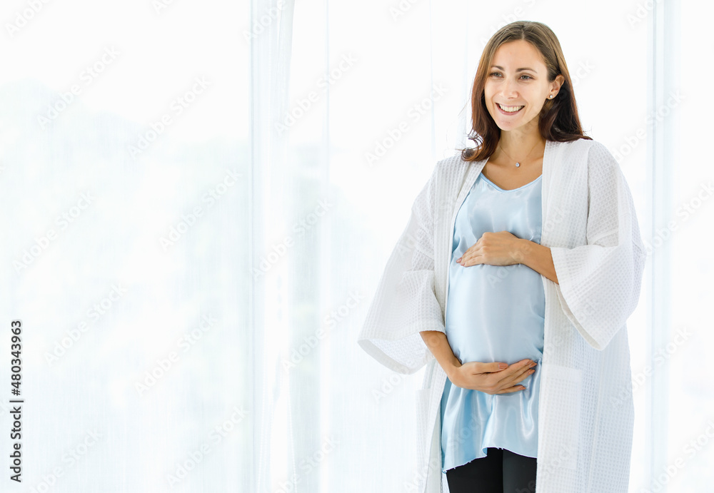 Lovely pregnant woman on maternity dress and nightgown tenderly embracing belly of unborn baby with care and smile as happy to become motherhood Lovely pregnant woman on maternity dress and nightgown tenderly embracing belly of unborn baby with care and smile as happy to become motherhood