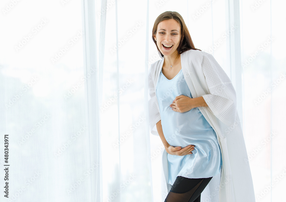 Lovely pregnant woman on maternity dress and nightgown tenderly embracing belly of unborn baby with care and smile as happy to become motherhood Lovely pregnant woman on maternity dress and nightgown tenderly embracing belly of unborn baby with care and smile as happy to become motherhood