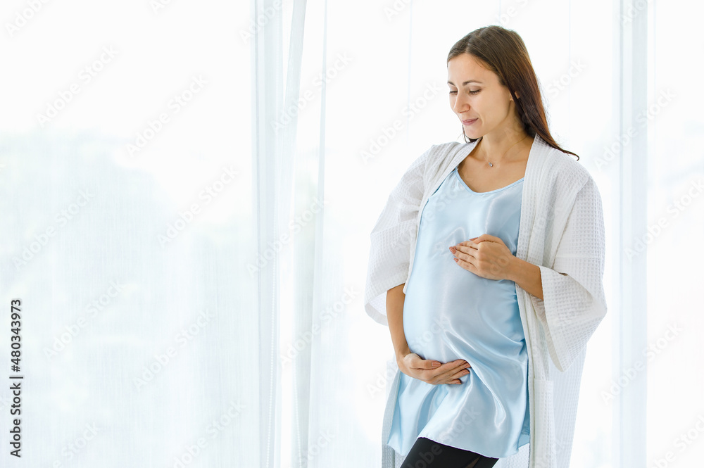 Lovely pregnant woman on maternity dress and nightgown tenderly embracing belly of unborn baby with care and smile as happy to become motherhood Lovely pregnant woman on maternity dress and nightgown tenderly embracing belly of unborn baby with care and smile as happy to become motherhood