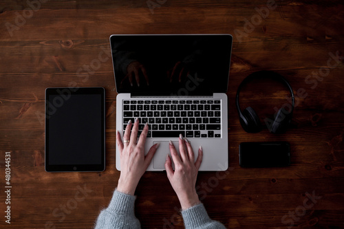 A laptop, a tablet, a phone and a pair of headphones arranged on a wooden table