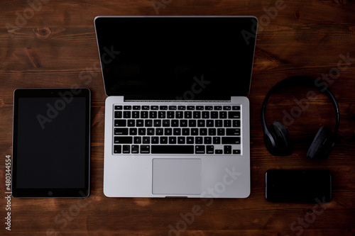 A laptop, a tablet, a phone and a pair of headphones arranged on a wooden table