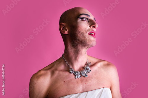 Portrait of emotive gender fluid middle-aged transgender gay man wearing necklace, isolated on pink background