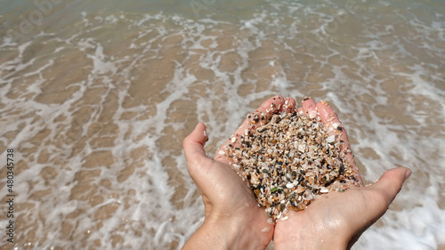 The girl holds a large sea sand in her hands against the background of the sea surf. Wet sand. Close-up. The concept of recreation, tourism and travel.
